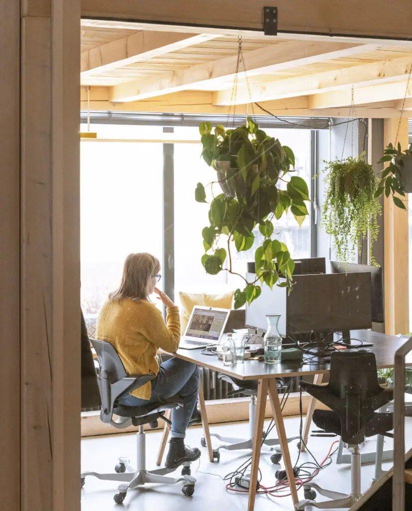 Eine Frau sitzt an Ihrem Arbeitsplatz auf einem Bürostuhl und blickt auf einen Laptop.